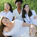 A multicultural group of women in white clothing posed outdoors in nature.
