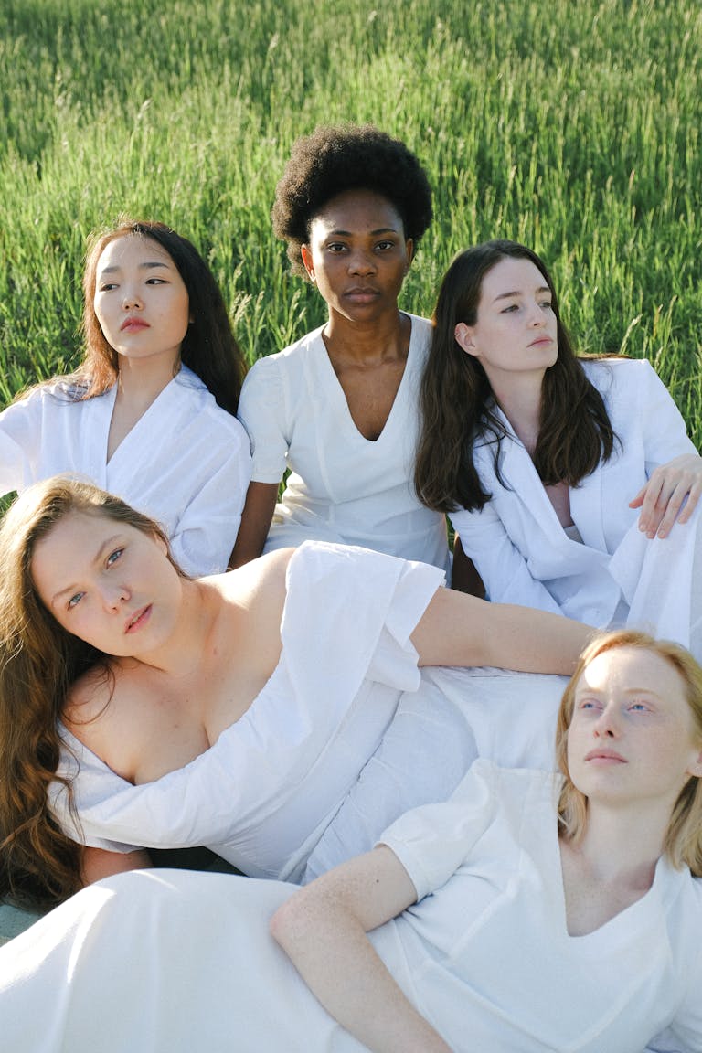 A multicultural group of women in white clothing posed outdoors in nature.