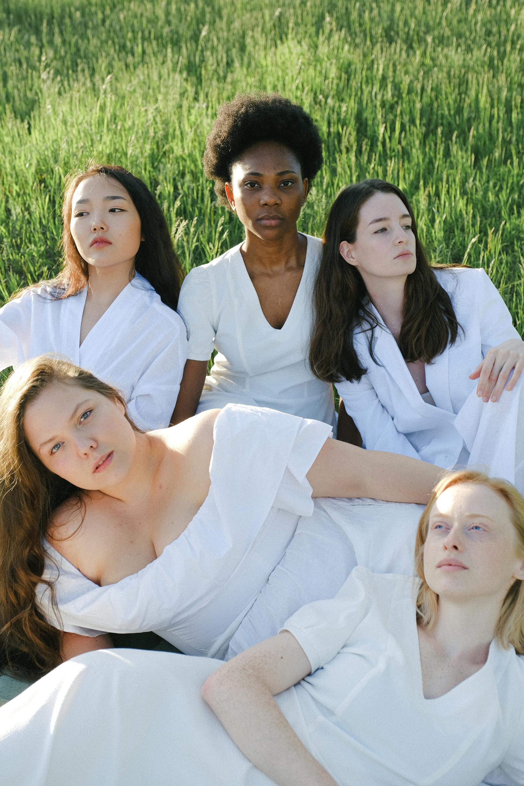 A multicultural group of women in white clothing posed outdoors in nature.