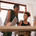 Four women in an office setting engaged in a lively creative discussion.